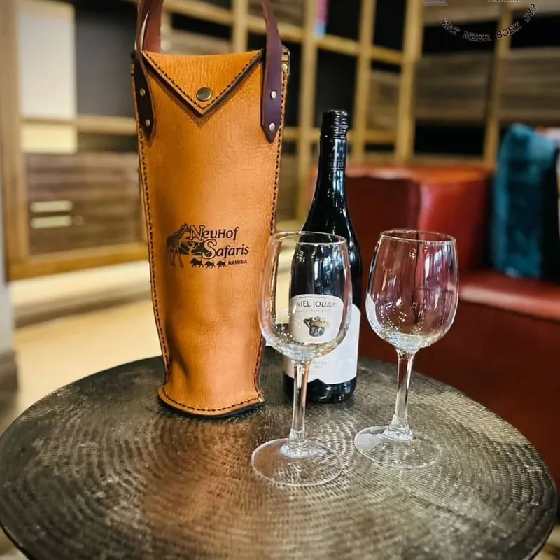 Leather wine caddy branded with a safari company logo, with wine and glasses